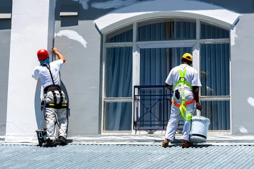 Two painters with safety gear working on a storefront with large windows