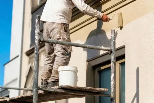 Painter on scaffolding applying a light coating to an exterior wall